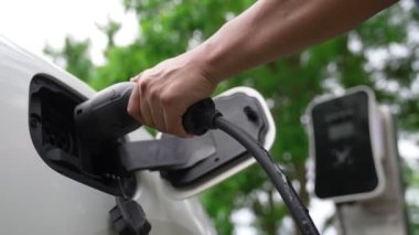 İlerici adam elektrikli aracına elektrik kablosu takıyor. Ev şarj istasyonundan EV arabası. Çevreyi korumak için temiz ve yenilenebilir enerji kullanan elektrikli bir araba. Çevre dostu otomobil.