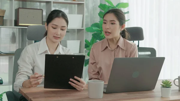 Enthusiastic office employees celebrate their success in office workplace. Colleagues collaborating at a table with a laptop and achieving achievement. Two businesswomen happy with their work.