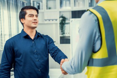 An engineer with a protective vest handshake with an investor in his office. Following a successful meeting, employee and employer form a partnership.