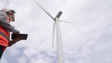 Gökyüzü arka planına sahip bir rüzgar türbini üzerinde çalışan mühendis. Yenilenebilir ve sürdürülebilir enerjinin gelecekteki üretimi için yenilikçi bir ideal. Rüzgar türbininden enerji üretimi.