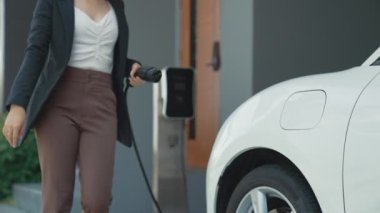 İlerici kadın evdeki elektrikli aracına şarj istasyonu fişi takıyor. EV otomobilleri çevreye yararlı temiz ve yeşil enerji kavramı sağlar.