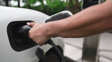 İlerici adam elektrikli aracına elektrik kablosu takıyor. Ev şarj istasyonundan EV arabası. Çevreyi korumak için temiz ve yenilenebilir enerji kullanan elektrikli bir araba. Çevre dostu otomobil.