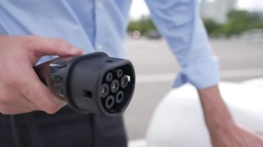 İlerici işadamı, şehir merkezinde dolaşmadan önce şarj cihazından elektrikli arabasına şarj prizi takıyor. Çevre dostu şarj edilebilir araba, sürdürülebilir ve temiz enerjiyle çalışıyor..