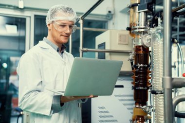 CBD yağ çıkarıcısının yanında dizüstü bilgisayarla çalışan eczacı bilim adamı ve tıbbi esrar ürünleri üretmek için kullanılan bilimsel bir makine.
