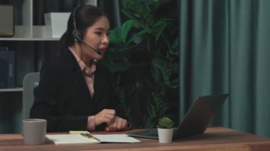 Kulaklık ve mikrofon takan iş kadını masasında çalışıyor ve dizüstü bilgisayar kullanıyor. Uzaktan kumandalı online toplantı için dizüstü bilgisayar kullanan hevesli kadın çalışanlar, ofiste iş videosu konferansı.