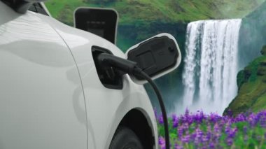 Elektrikli araba, doğal ortam, şelale ve akış arkaplanındaki şarj istasyonundan enerji yüklüyor. Yenilenebilir enerji kaynaklı EV otomobillerin enerji sürdürülebilirliği kavramı.