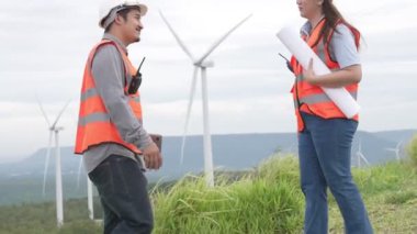 Erkek ve kadın mühendisler kırsal kesimdeki bir tepenin tepesinde ya da dağda rüzgar çiftliğinde çalışıyorlar. Yenilenebilir ve sürdürülebilir enerjinin gelecekteki üretimi için yenilikçi idealler.