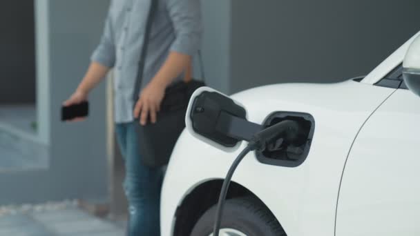 男は電気自動車の充電器を自分の家に取り外します 先進的なライフスタイルにおける電気自動車の使用の概念は 清潔で健康的な環境に貢献します — ストック動画