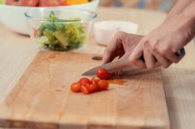 Close up hands holding a knife preparing a contented meal. Sliced tomatoes and other vegetables on the glass dish.