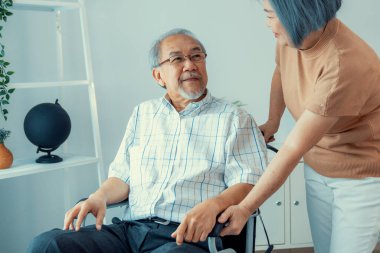 Senior wife giving support to her husband in his wheelchair with love, contented pensioner life. A senior couple is understanding and smiling at each other.