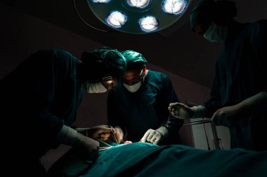 Steril ameliyathanedeki hastaya ameliyat yapan cerrahi ekip. Bir lambanın yaktığı ameliyathanede, profesyonel ve kendinden emin bir cerrahi ekip bilinçsiz bir hastaya tıbbi bakım sağlar..