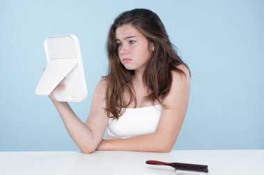 Beautiful girl feel sad, worry about her damaged hair with isolated background. Concept of dry lifeless hair. Young charming girl hold her tangled hair and look at it with worried expression.