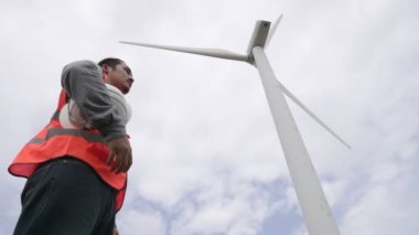 Gökyüzü arka planına sahip bir rüzgar türbini üzerinde çalışan mühendis. Yenilenebilir ve sürdürülebilir enerjinin gelecekteki üretimi için yenilikçi bir ideal. Rüzgar türbininden enerji üretimi.