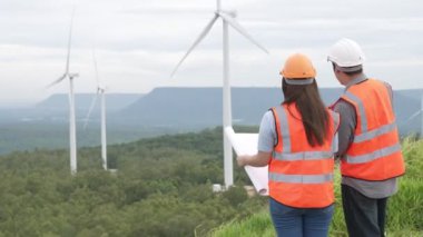Erkek ve kadın mühendisler kırsal kesimdeki bir tepenin tepesinde ya da dağda rüzgar çiftliğinde çalışıyorlar. Yenilenebilir ve sürdürülebilir enerjinin gelecekteki üretimi için yenilikçi idealler.