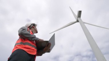 Gökyüzü arka planına sahip bir rüzgar türbini üzerinde çalışan mühendis. Yenilenebilir ve sürdürülebilir enerjinin gelecekteki üretimi için yenilikçi bir ideal. Rüzgar türbininden enerji üretimi.