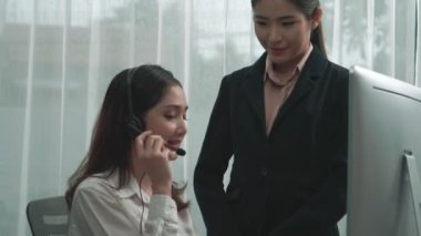 Hevesli Asyalı bayan yönetici yeni çalışana ofiste nasıl verimli müşteri hizmetleri operatörü olunacağını öğretiyor. Genç bayan çağrı merkezi kulaklık kullanarak müşteri desteği sağlıyor..