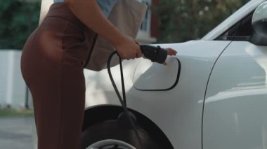 İlerici kadın evdeki elektrikli aracına şarj istasyonu fişi takıyor. EV otomobilleri çevreye yararlı temiz ve yeşil enerji kavramı sağlar.