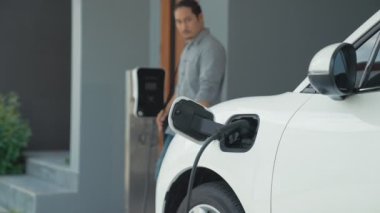 Adamın biri evinde elektrikli araç şarj aletinin fişini çekiyor. İlerici bir yaşam tarzında elektrikli araçların kullanımı, temiz ve sağlıklı bir çevreye katkıda bulunur..