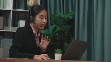 Kulaklık ve mikrofon takan iş kadını masasında çalışıyor ve dizüstü bilgisayar kullanıyor. Uzaktan kumandalı online toplantı için dizüstü bilgisayar kullanan hevesli kadın çalışanlar, ofiste iş videosu konferansı.