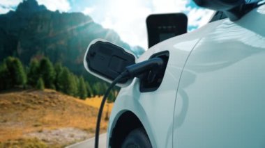 Elektro jeneratör sürücüsüyle enerji sürdürülebilir araba gücü, şarj istasyonunda şarj edilen batarya, ilerici seyahat konsepti için dağ zeminine sahip. Temiz ortamın sembolü olarak doğadaki EV otomobil.