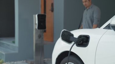 Adamın biri evinde elektrikli araç şarj aletinin fişini çekiyor. İlerici bir yaşam tarzında elektrikli araçların kullanımı, temiz ve sağlıklı bir çevreye katkıda bulunur..