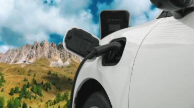 Temiz çevre için temiz enerjinin yol açtığı ilerici elektrikli araba kavramının arka planı olarak dağın tepesinde bulutun zaman kavramının yer aldığı doğal manzara. EV araba şarj istasyonunda şarj oluyor..