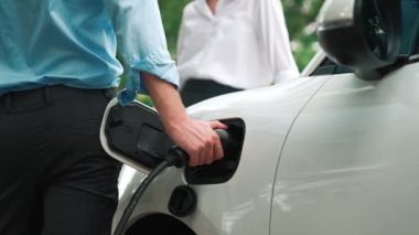 İlerici işadamı ve iş kadını, şehir merkezinde dolaşmadan önce şarj cihazını şarj istasyonundan elektrikli arabaya takıyor. Çevre dostu şarj edilebilir araba temiz enerjiyle çalışıyor..