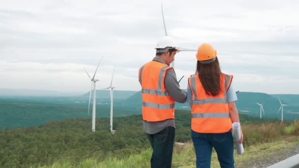 田舎の丘や山の上の風力発電所で働く男性と女性のエンジニア 再生可能エネルギー 持続可能なエネルギーの将来の生産のための進歩的な理想 — ストック動画