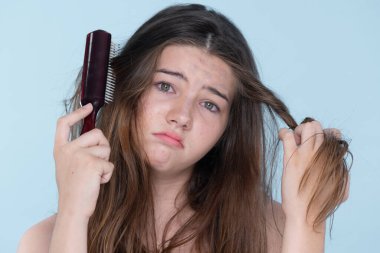 Beautiful girl feel sad, worry about her damaged hair with isolated background. Concept of dry lifeless hair. Young charming girl hold her tangled hair and look at it with worried expression.