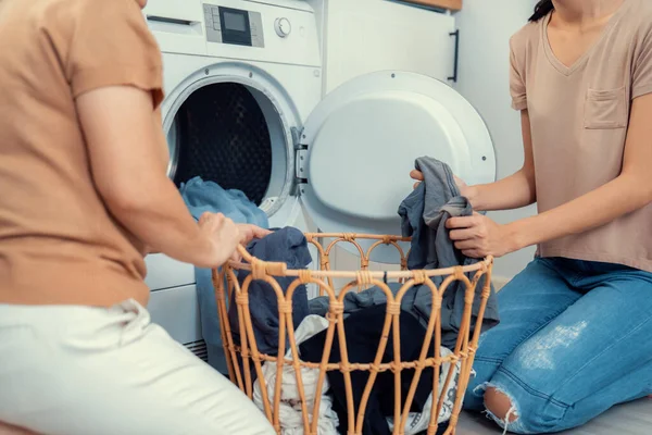 Daughter and mother working together to complete their household chores near the washing machine in a happy and contented manner. Mother and daughter doing the usual tasks in the house.