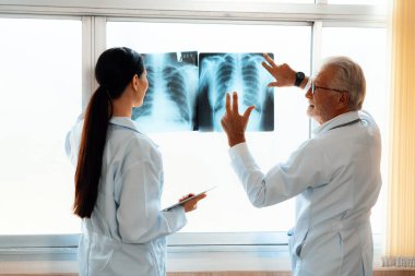 Hastane steril odasında, iki profesyonel radyolog tıbbi röntgen teşhisi için bir radyografı tutuyor ve inceliyor. Acemi doktor tecrübeli yaşlı doktordan hasta durumuyla ilgili tavsiye ister..