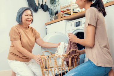 Daughter and mother working together to complete their household chores near the washing machine in a happy and contented manner. Mother and daughter doing the usual tasks in the house.