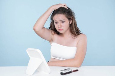 Young charming teenager girl worry about her face pimples on mirror for skincare and acne problem concept. Stress young girl squeezing pimples and pointing fingers on acne on her face.