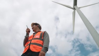 Gökyüzü arka planına sahip bir rüzgar türbini üzerinde çalışan mühendis. Yenilenebilir ve sürdürülebilir enerjinin gelecekteki üretimi için yenilikçi bir ideal. Rüzgar türbininden enerji üretimi.