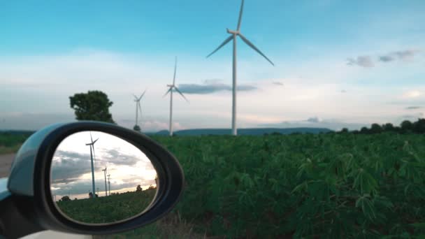 利用风力涡轮机的绿色和可再生能源在充电站充电的电动汽车侧面镜中反映出风力涡轮机的渐进式未来能源基础设施概念 — 图库视频影像