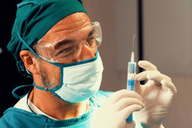 Cerrah steril ameliyathanede cerrahi prosedür için tıbbi şişeden şırınga dolduruyor. Ameliyat için koruyucu giysisi olan doktor hastasına anestezi iğnesi hazırlayın.