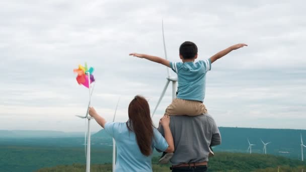 風力タービン農場で彼らの時間を楽しんで進歩的な幸せな家族の概念 水平線に丘や山を持つ国側の風力発電機による風力発電機 — ストック動画