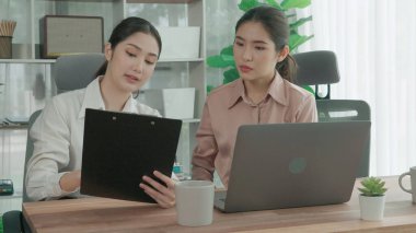 Ofis çalışma alanında birlikte çalışan iki genç hevesli iş kadını. Genç meslektaşlar tartışırken ve dizüstü bilgisayar kullanırken. Modern ofis çalışanları masada birlikte oturuyorlar..