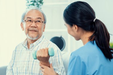 Contented senior patient doing physical therapy with the help of his caregiver. Senior physical therapy, physiotherapy treatment, nursing home for the elderly