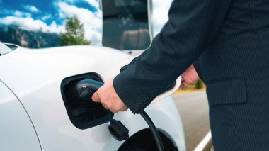 İlerici adam, yeşil çevre için yenilenebilir ve temiz enerjiyle çalışan EV otomobili hedefine ulaşmadan önce uzak bölgedeki şarj istasyonundan enerjiyi şarj etmek için duruyor.