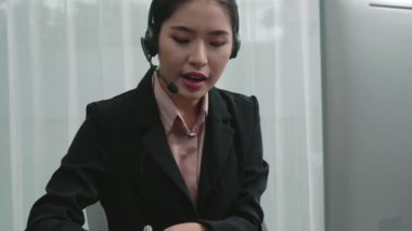 Masasında dizüstü bilgisayarla çalışan kulaklık ve mikrofon takan Asyalı müşteri destek operatörü. Hevesli kadın çalışanlar müşteri hizmetleri sunuyor, destekleyici çağrı merkezi temsilcisi müşterilere yardım ediyor.
