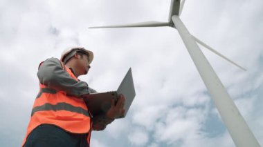 Gökyüzü arka planına sahip bir rüzgar türbini üzerinde çalışan mühendis. Yenilenebilir ve sürdürülebilir enerjinin gelecekteki üretimi için yenilikçi bir ideal. Rüzgar türbininden enerji üretimi.
