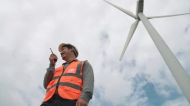 Gökyüzü arka planına sahip bir rüzgar türbini üzerinde çalışan mühendis. Yenilenebilir ve sürdürülebilir enerjinin gelecekteki üretimi için yenilikçi bir ideal. Rüzgar türbininden enerji üretimi.