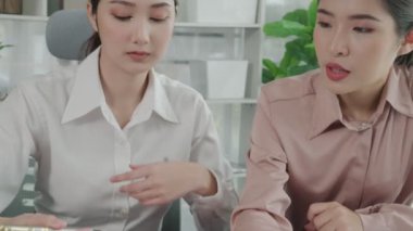 Ofis masasında çalışan iki hevesli genç iş kadını, veri tablosu raporlarıyla birlikte. Genç meslektaşlar istatistik veri kağıdı planları ve stratejisini tartışıyor ve analiz ediyorlar.