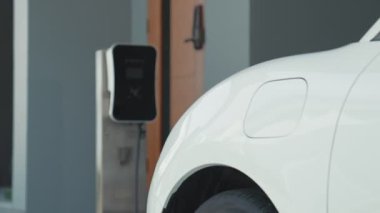 İlerici adam evindeki elektrikli aracın aküsüne emisyonsuz güç bağlantısı kuruyor. Elektrikli araç elektrik istasyonundan EV araba aküsüne kabloyla şarj oluyor.