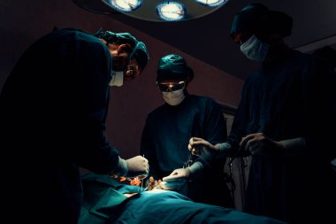 Steril ameliyathanedeki hastaya ameliyat yapan cerrahi ekip. Bir lambanın yaktığı ameliyathanede, profesyonel ve kendinden emin bir cerrahi ekip bilinçsiz bir hastaya tıbbi bakım sağlar..