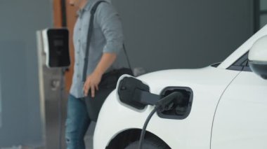 Adamın biri evinde elektrikli araç şarj aletinin fişini çekiyor. İlerici bir yaşam tarzında elektrikli araçların kullanımı, temiz ve sağlıklı bir çevreye katkıda bulunur..