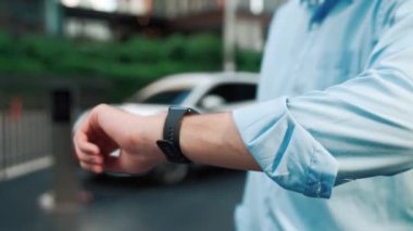 Takım elbiseli, hırslı bir işadamı elektrik kablosu ve yenilenebilir enerji enerjili bir elektrikli araçla şarj istasyonunda dururken elektrikli aracına yaslanıyor..