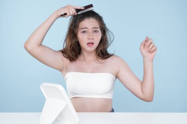 Beautiful girl feel sad, worry about her damaged hair with isolated background. Concept of dry lifeless hair. Young charming girl hold her tangled hair and look at it with worried expression.