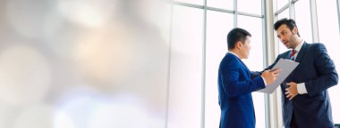 Geniş görüşlü toplantı odasında iki iş adamı proje stratejisini konuşuyor. İş adamı modern işyerindeki meslektaşıyla proje planlamasını tartıştı .